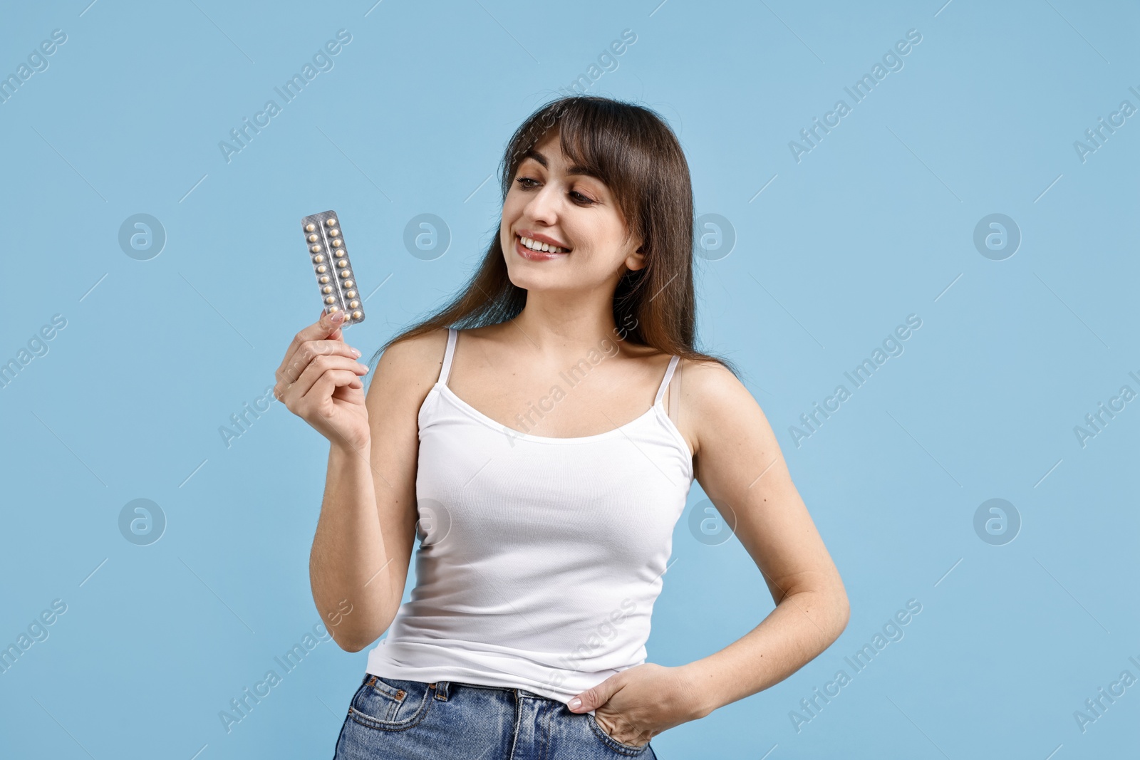 Photo of Smiling woman with blister of contraceptive pills on light blue background