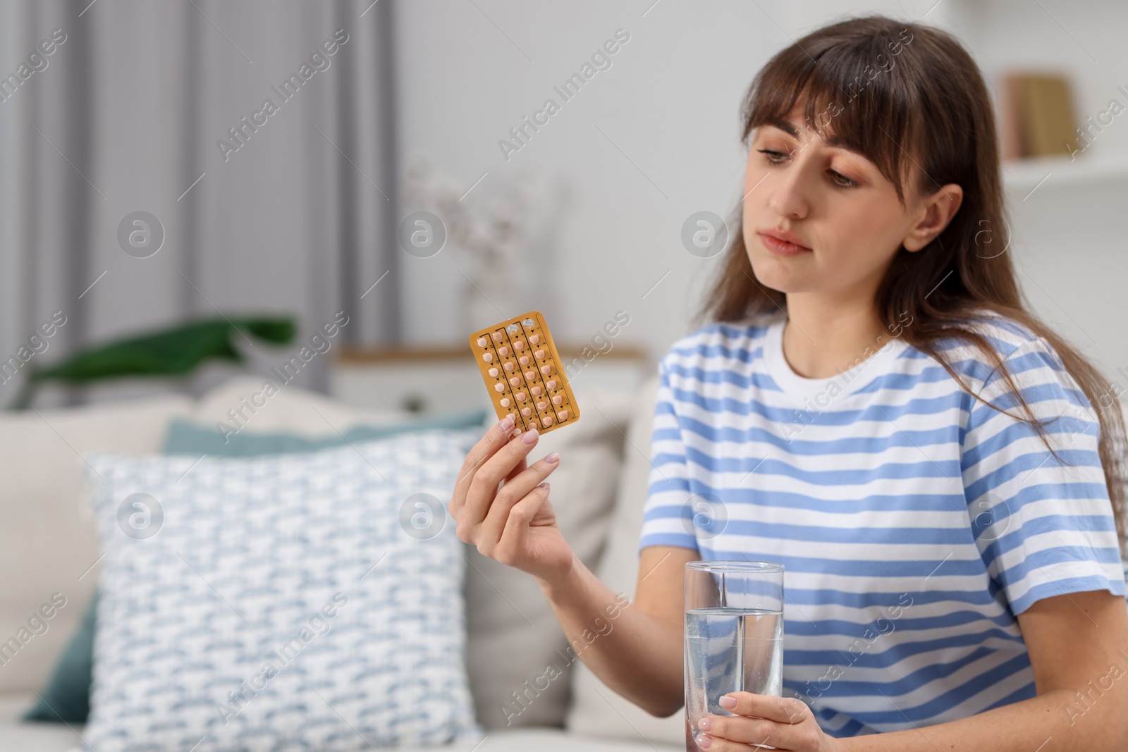 Photo of Woman with contraceptive pills and glass of water on sofa at home. Space for text