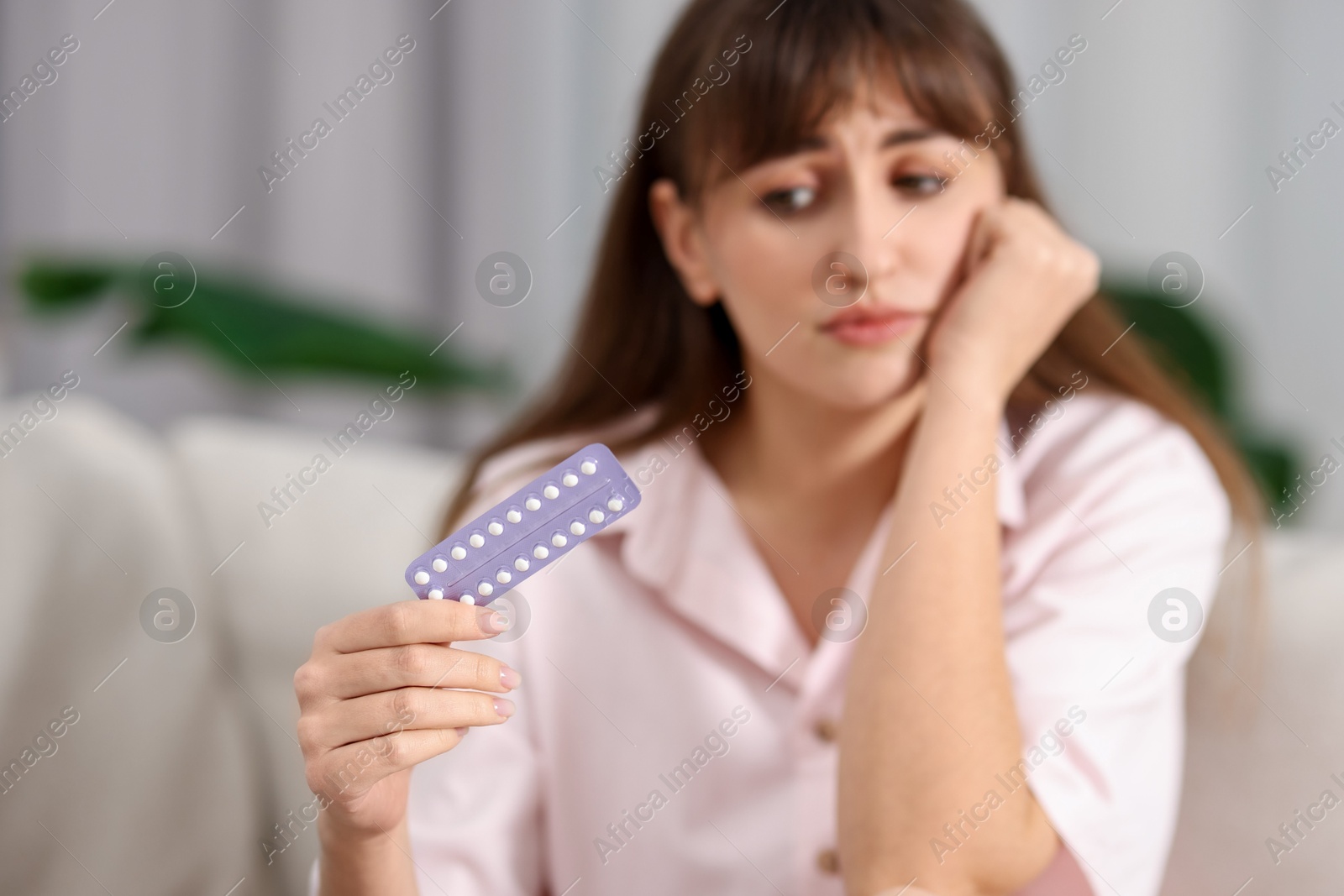 Photo of Upset woman with blister of contraceptive pills indoors, selective focus