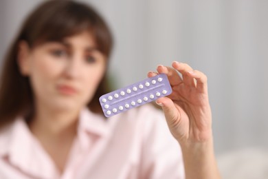 Photo of Woman with blister of contraceptive pills indoors, selective focus