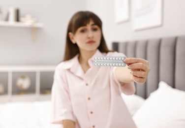 Photo of Woman with blister of contraceptive pills on bed indoors, selective focus