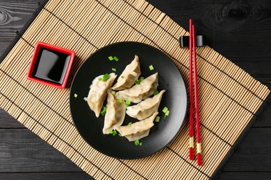 Photo of Delicious gyoza dumplings with chives served on black wooden table, top view