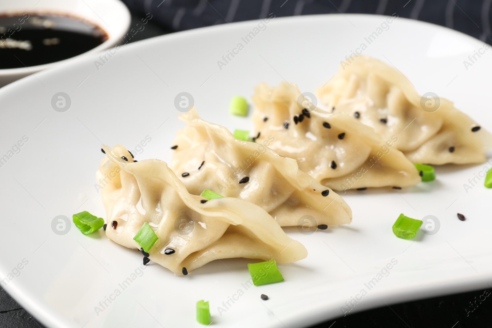 Photo of Delicious gyoza dumplings with chives and sesame seeds served on black table, closeup