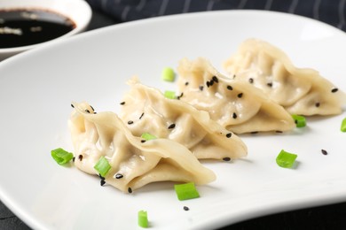 Photo of Delicious gyoza dumplings with chives and sesame seeds served on black table, closeup