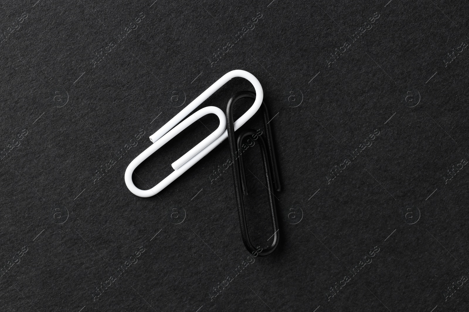 Photo of Two paper clips on black background, top view