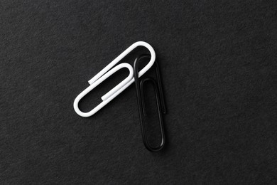 Photo of Two paper clips on black background, top view