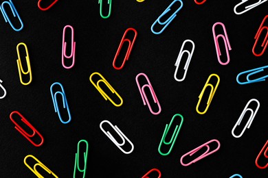 Photo of Colorful paper clips on black background, flat lay