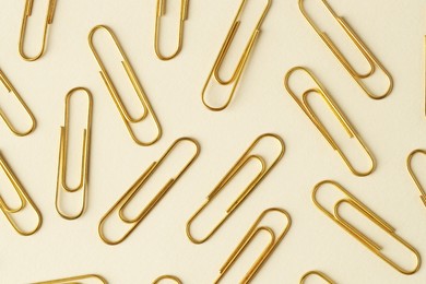 Golden paper clips on beige background, flat lay