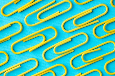 Many paper clips on light blue background, flat lay