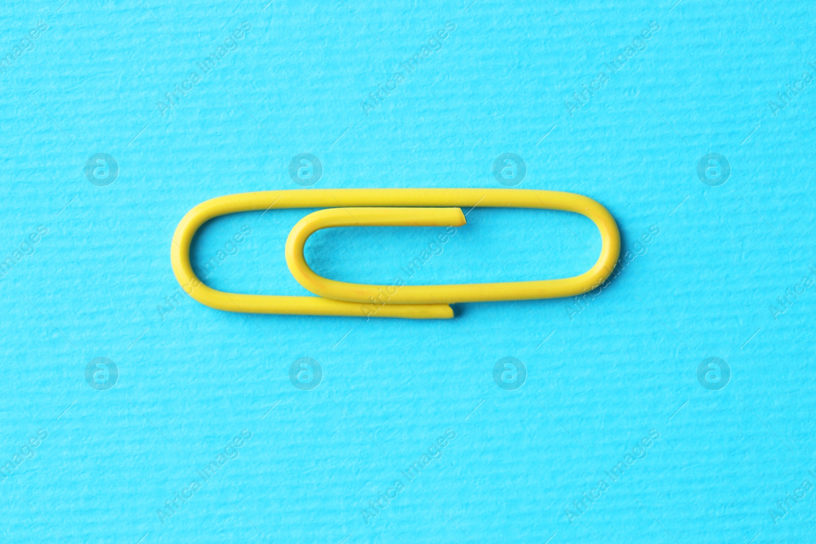 Photo of One paper clip on light blue background, top view