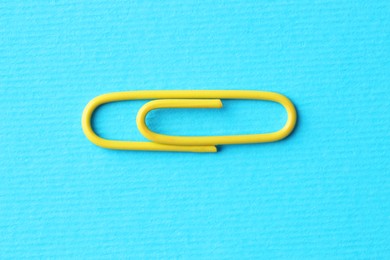 Photo of One paper clip on light blue background, top view