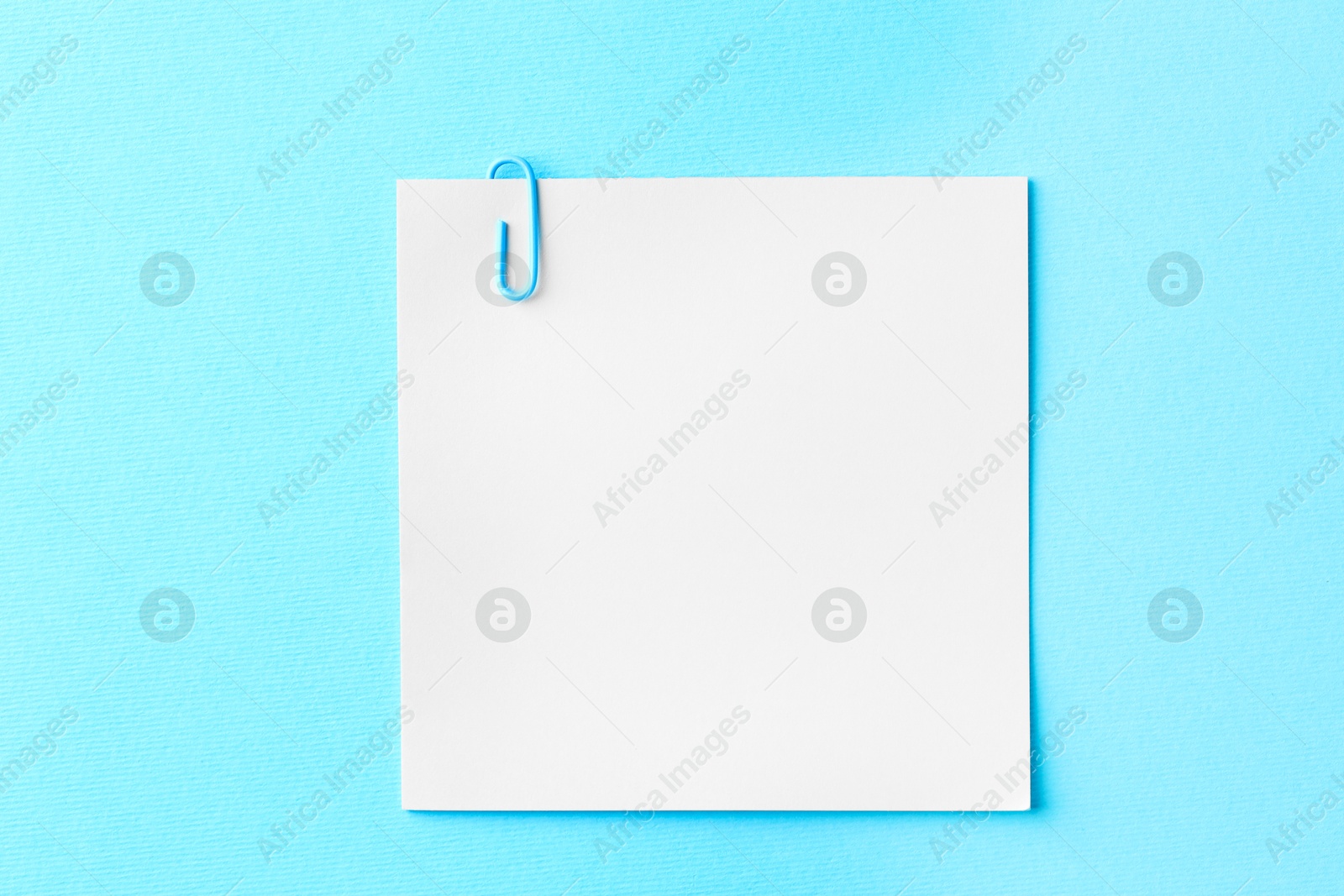 Photo of Paper note with clip on light blue background, top view. Space for text