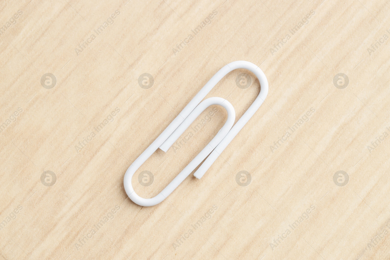 Photo of One white paper clip on wooden table, top view