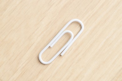 Photo of One white paper clip on wooden table, top view