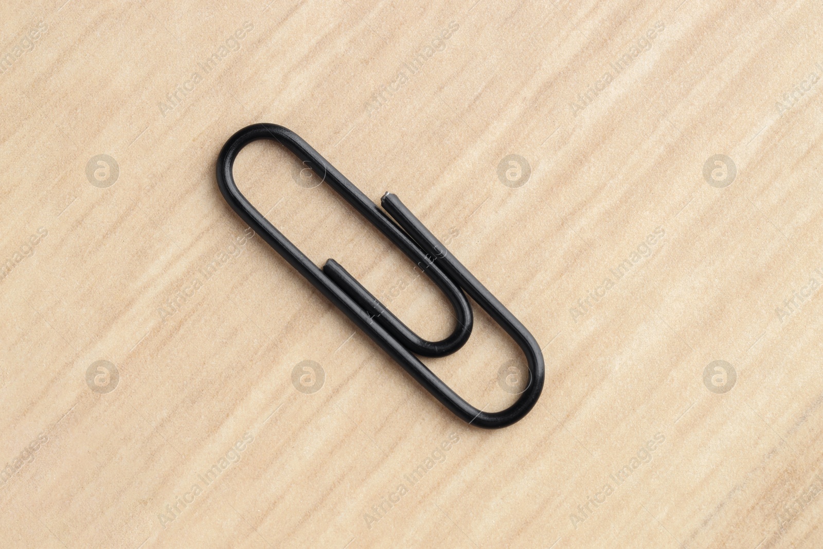 Photo of One black paper clip on wooden table, top view