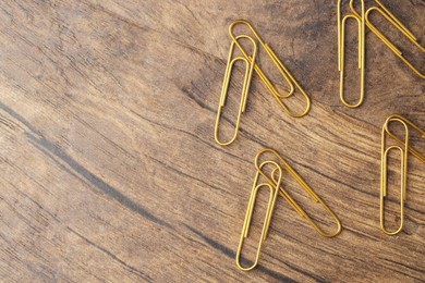 Many golden paper clips on wooden table, flat lay. Space for text