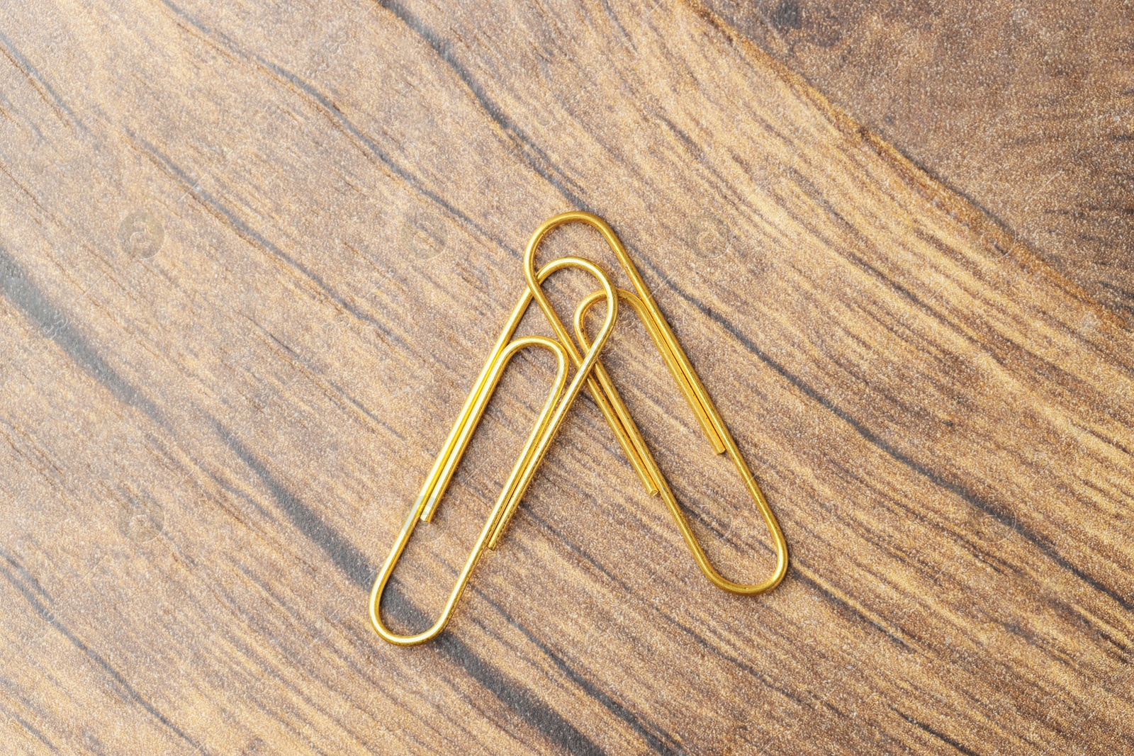 Photo of Two golden paper clips on wooden table, top view