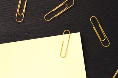 Photo of Paper note and many golden clips on black wooden table, flat lay