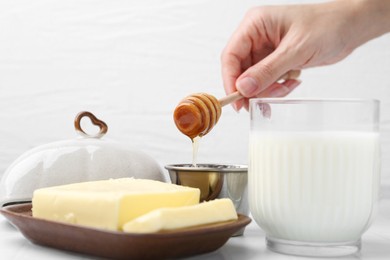 Photo of Woman with honey dipper, closeup. Fresh milk in glass and butter on white tiled table