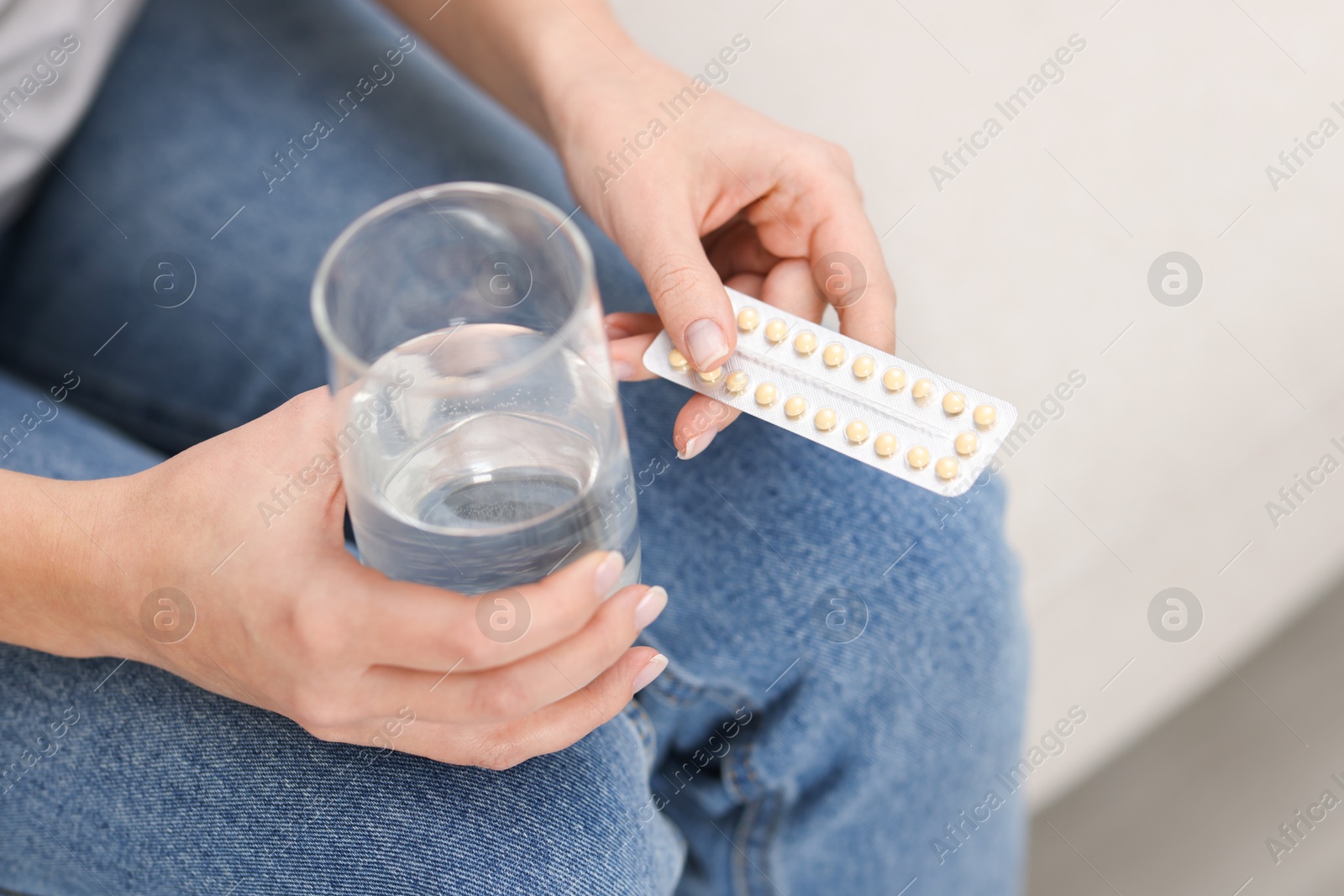 Photo of Woman with contraceptive pills and glass of water on sofa, closeup