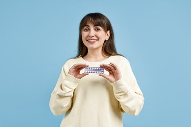 Photo of Smiling woman with blister of contraceptive pills on light blue background