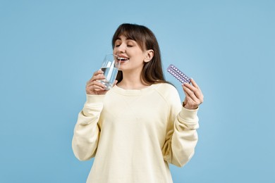 Photo of Young woman with contraceptive pills drinking water on light blue background