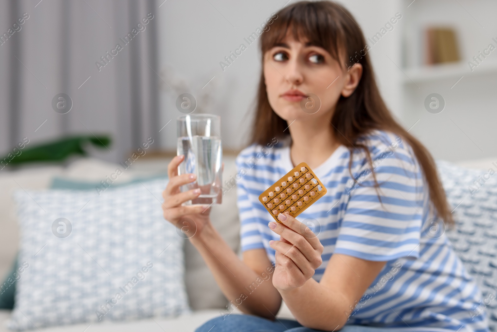 Photo of Woman with contraceptive pills and glass of water on sofa at home. Space for text