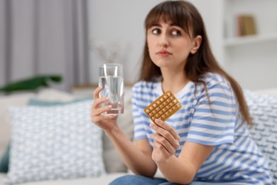 Photo of Woman with contraceptive pills and glass of water on sofa at home. Space for text