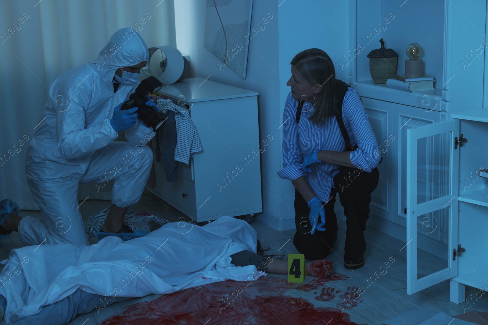 Photo of Forensic experts working at crime scene with dead woman's body indoors