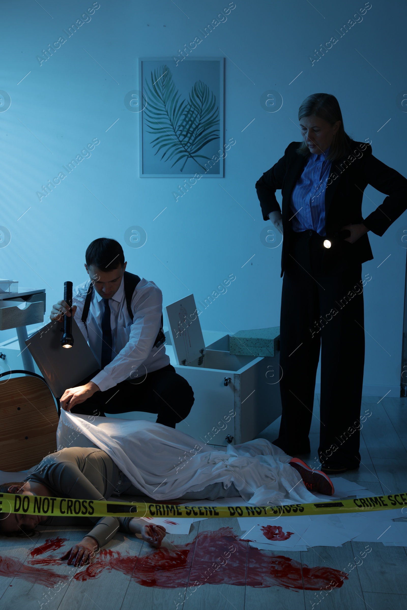 Photo of Forensic experts working at crime scene with dead woman's body indoors