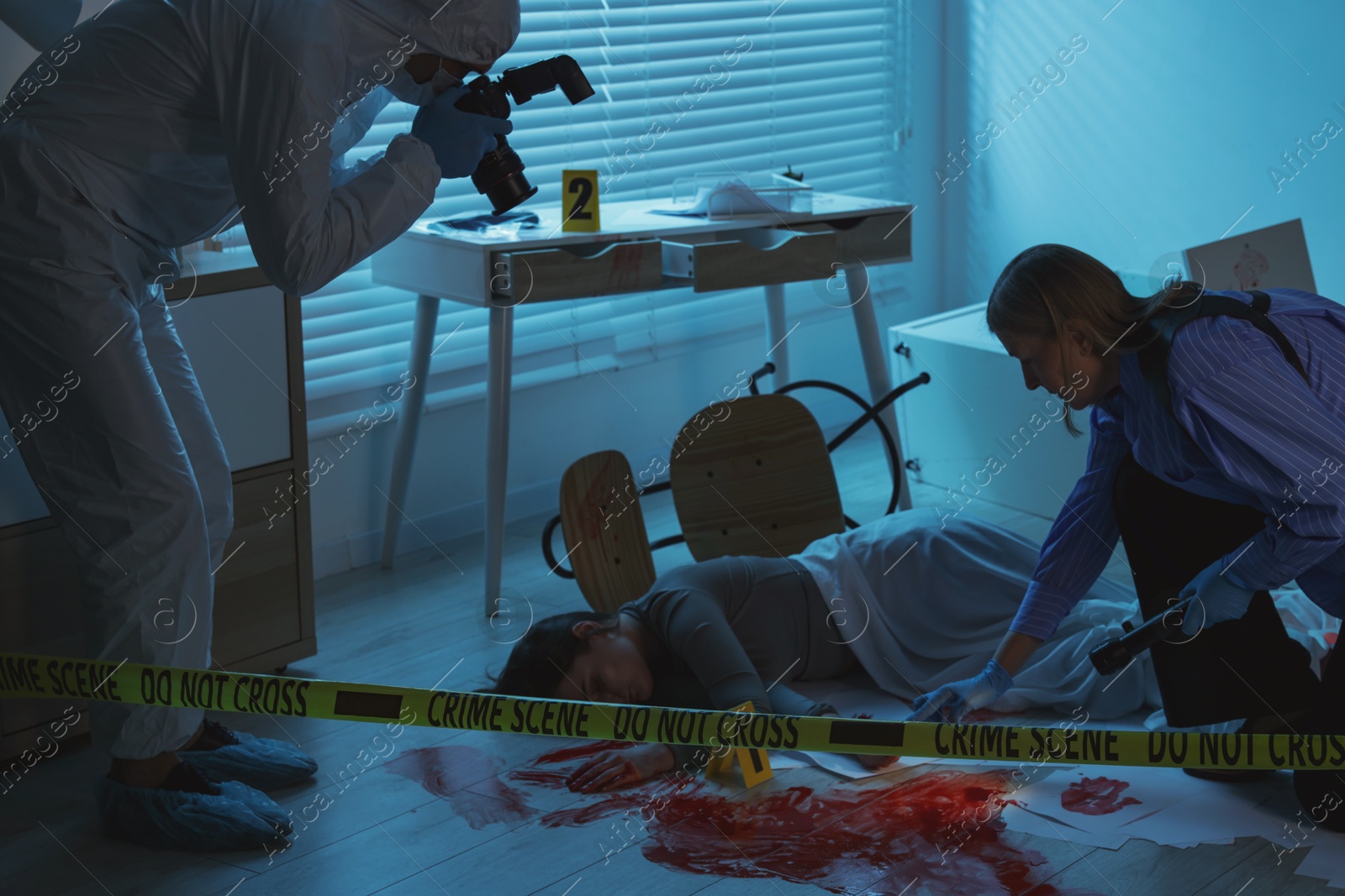 Photo of Forensic experts working at crime scene with dead woman's body indoors