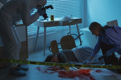 Photo of Forensic experts working at crime scene with dead woman's body indoors