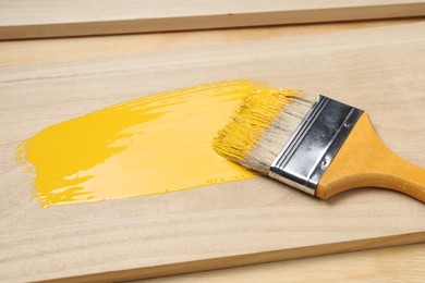 Photo of Brush with yellow paint on wooden plank, closeup