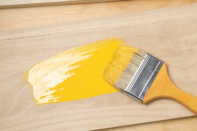 Photo of Brush with yellow paint on wooden plank, top view