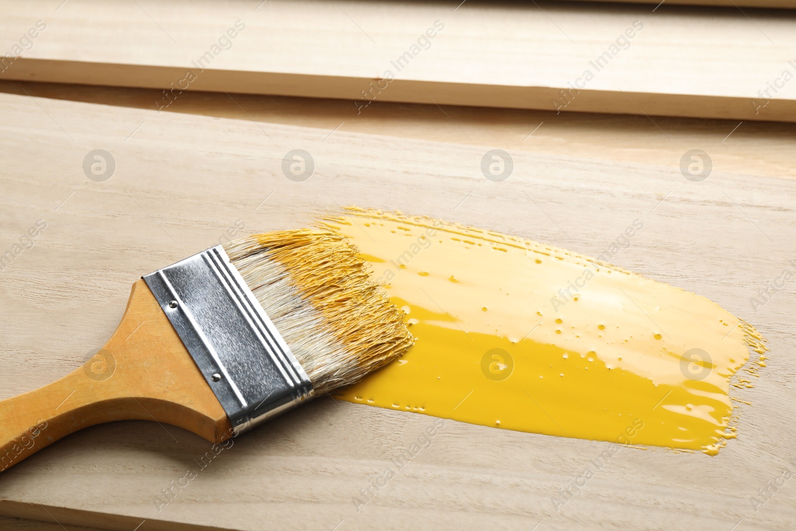 Photo of Brush with yellow paint on wooden plank, closeup