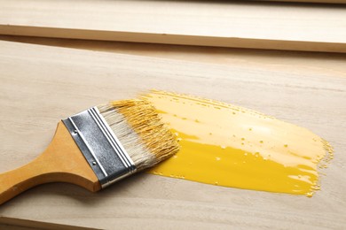 Brush with yellow paint on wooden plank, closeup