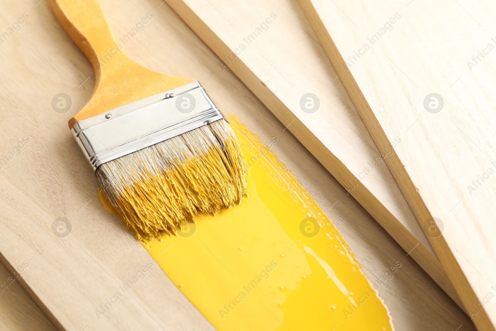 Photo of Brush with yellow paint on wooden plank, closeup