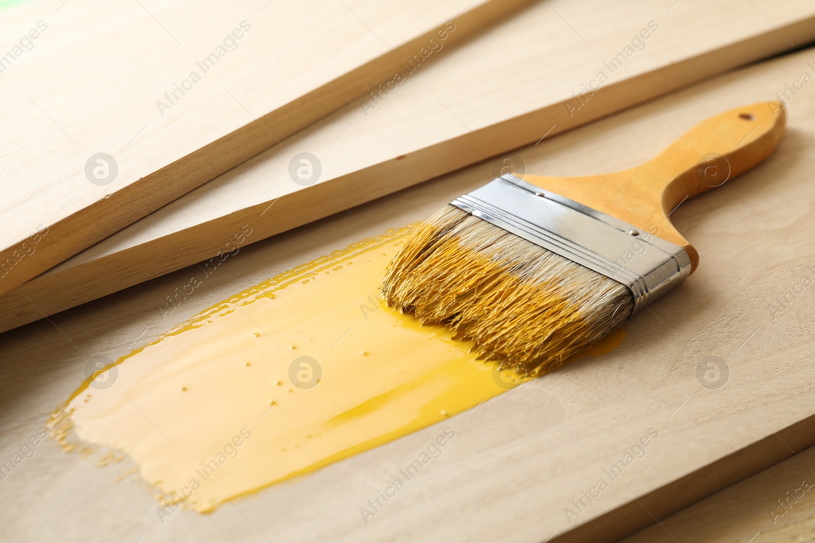 Photo of Brush with yellow paint on wooden plank, closeup