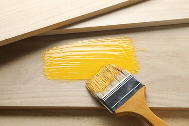 Brush with yellow paint on wooden planks, above view