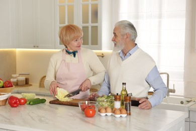 Senior couple cooking together at table in kitchen