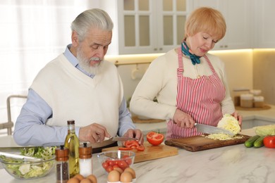 Senior couple cooking together at table in kitchen