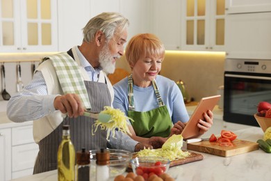 Photo of Senior couple using tablet while cooking together in kitchen