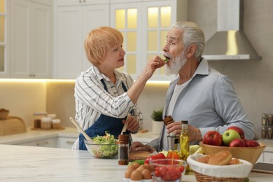 Photo of Senior couple feeding each other while cooking in kitchen