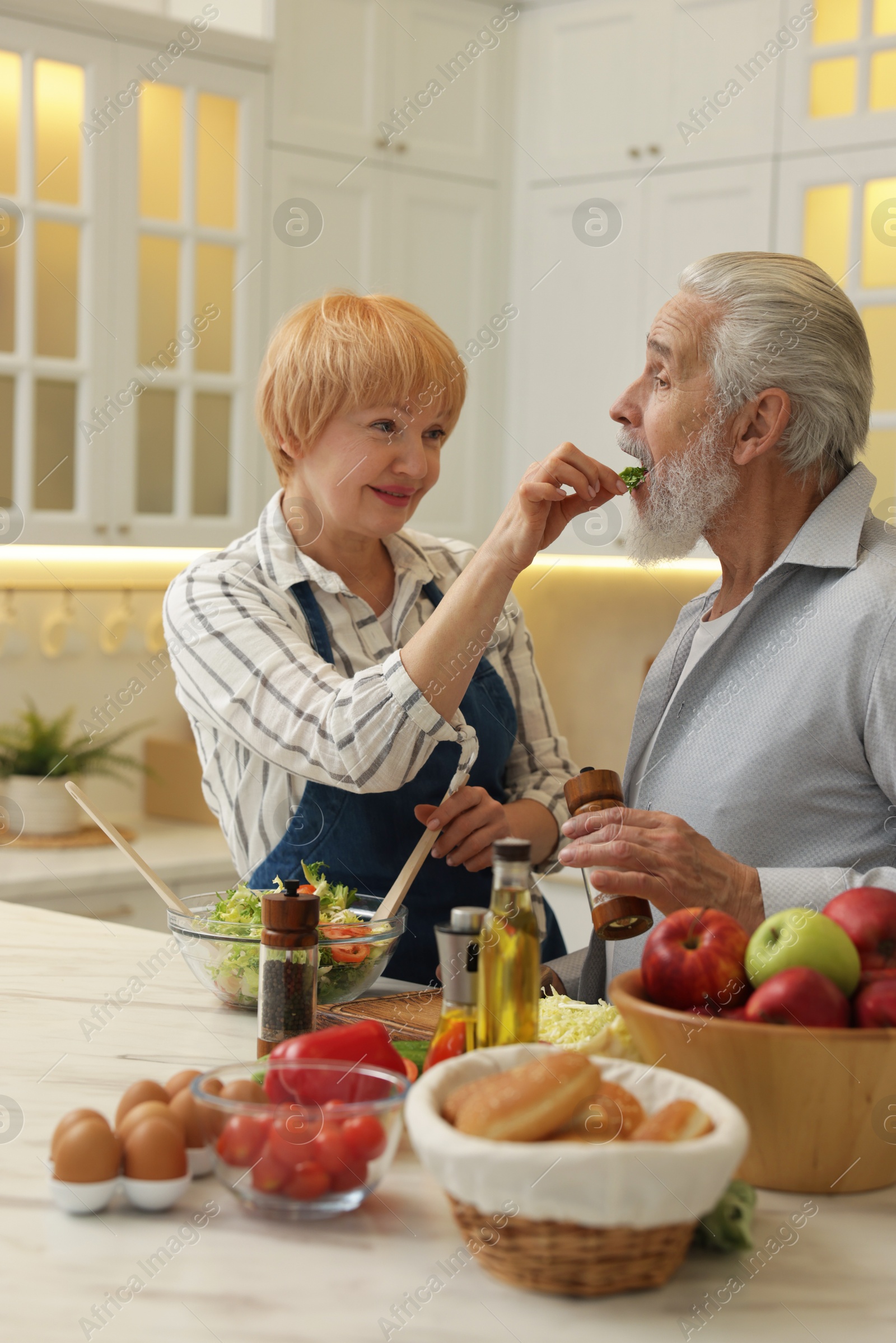 Photo of Senior couple feeding each other while cooking in kitchen