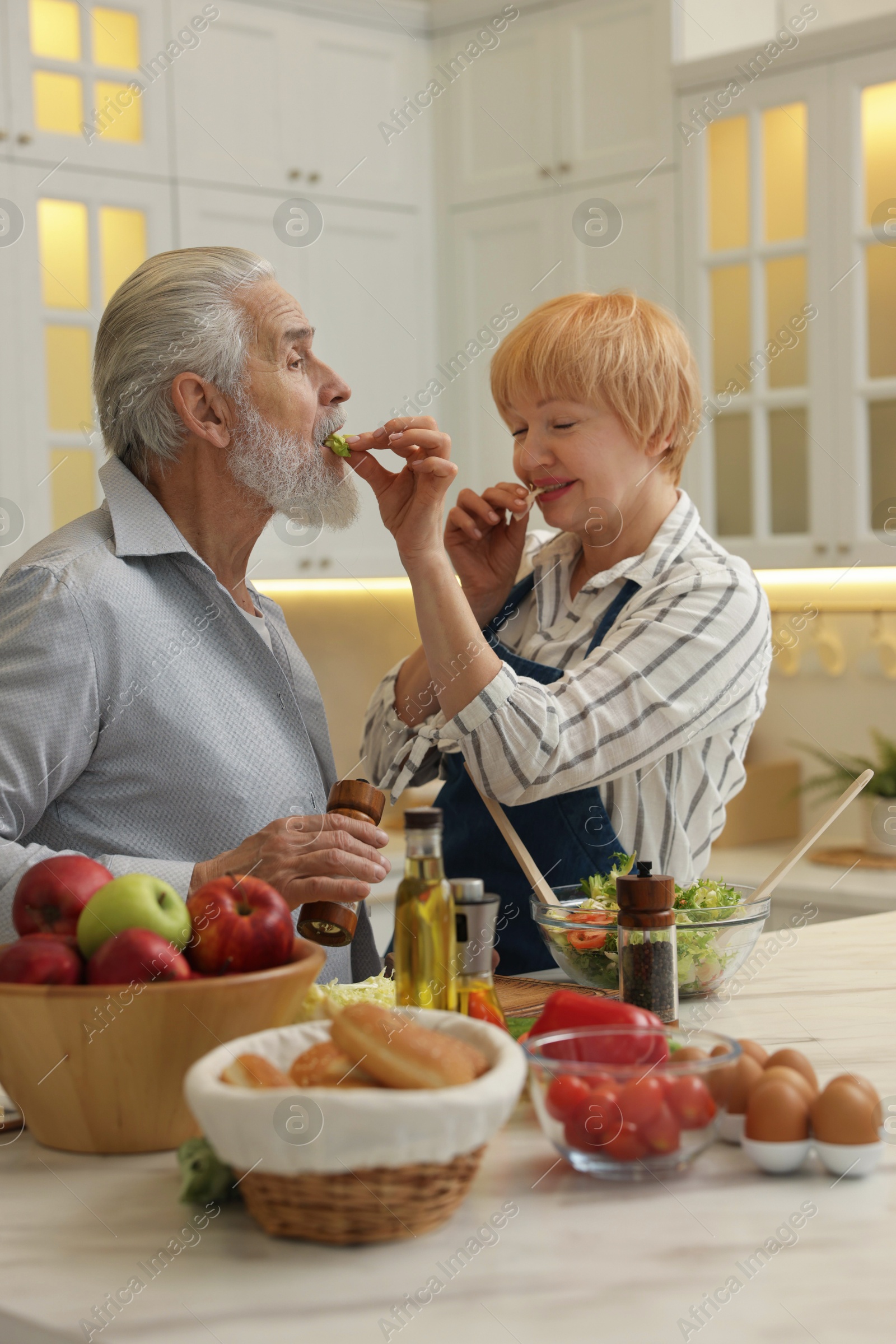 Photo of Senior couple feeding each other while cooking in kitchen