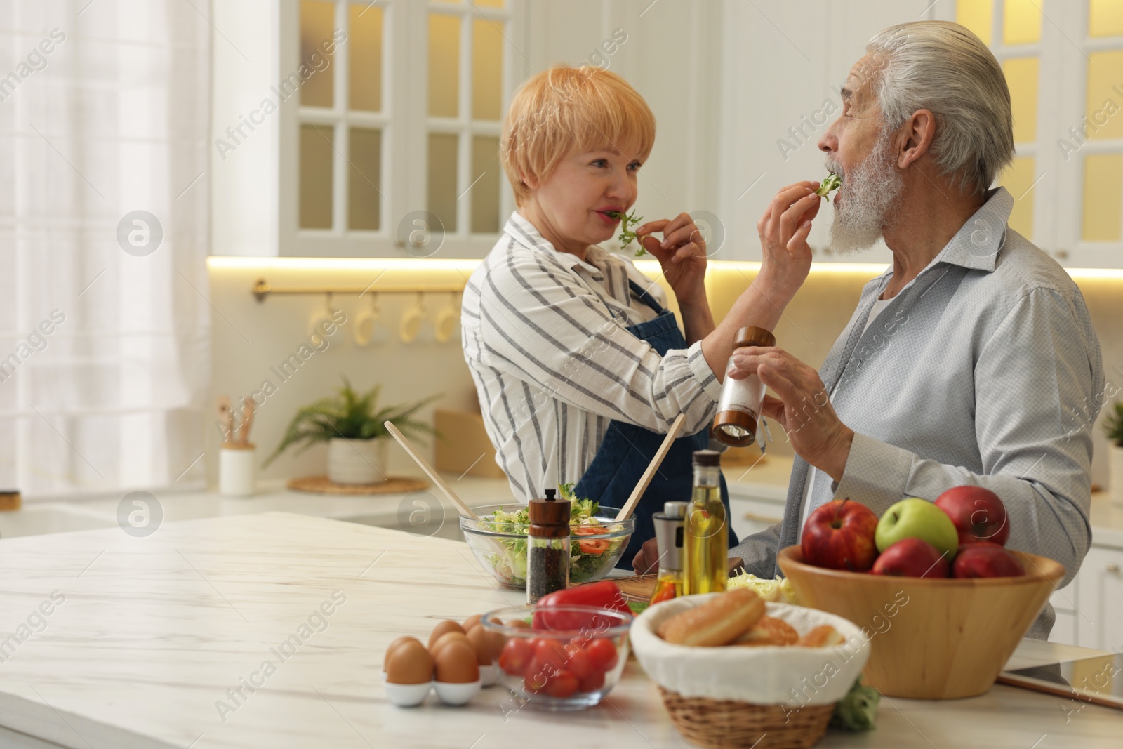 Photo of Senior couple feeding each other while cooking in kitchen