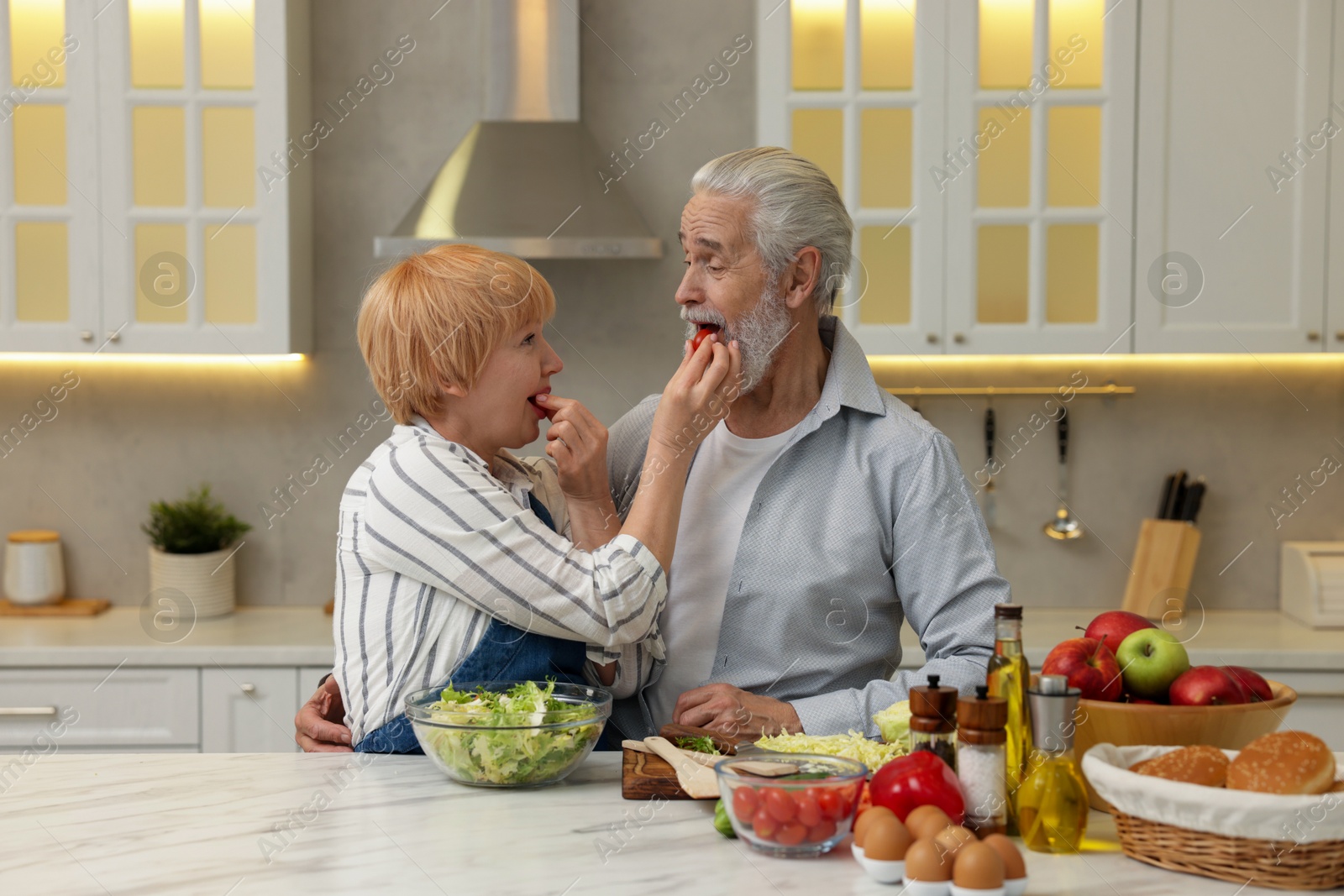 Photo of Senior couple feeding each other while cooking in kitchen