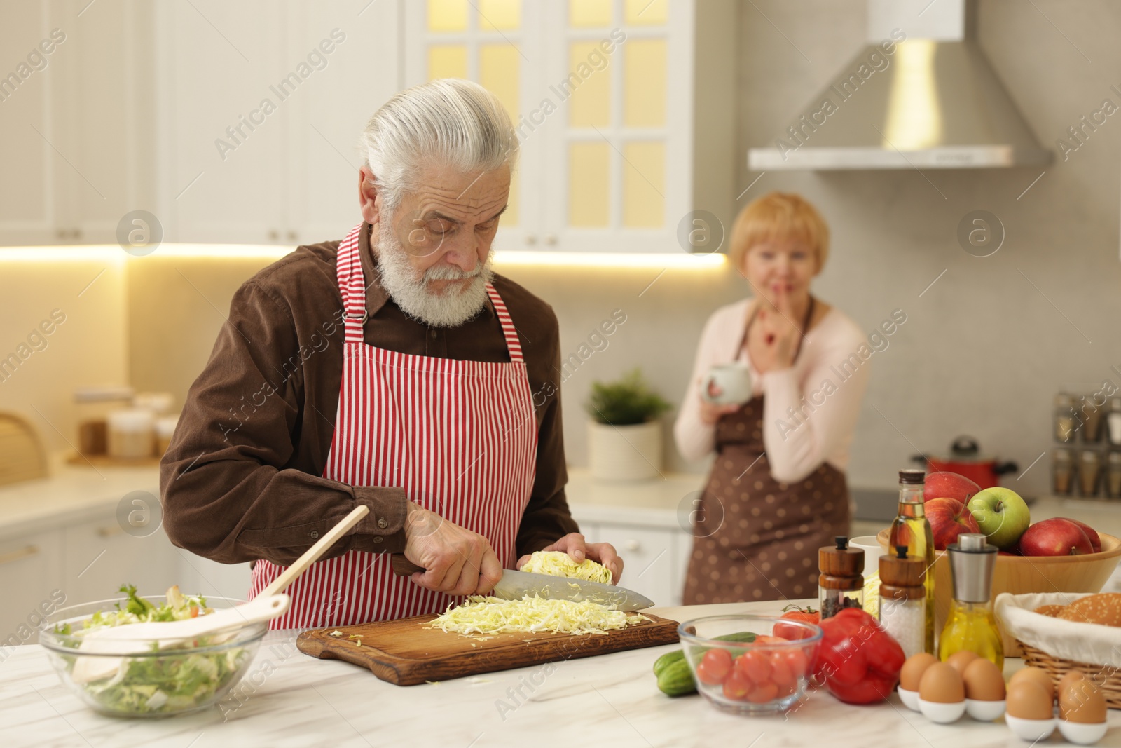 Photo of Senior woman looking at her husband cooking in kitchen, selective focus