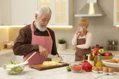 Photo of Senior woman looking at her husband cooking in kitchen, selective focus