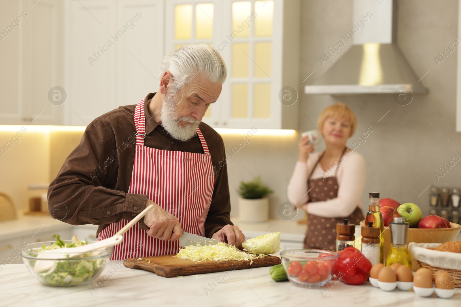 Photo of Senior woman looking at her husband cooking in kitchen, selective focus